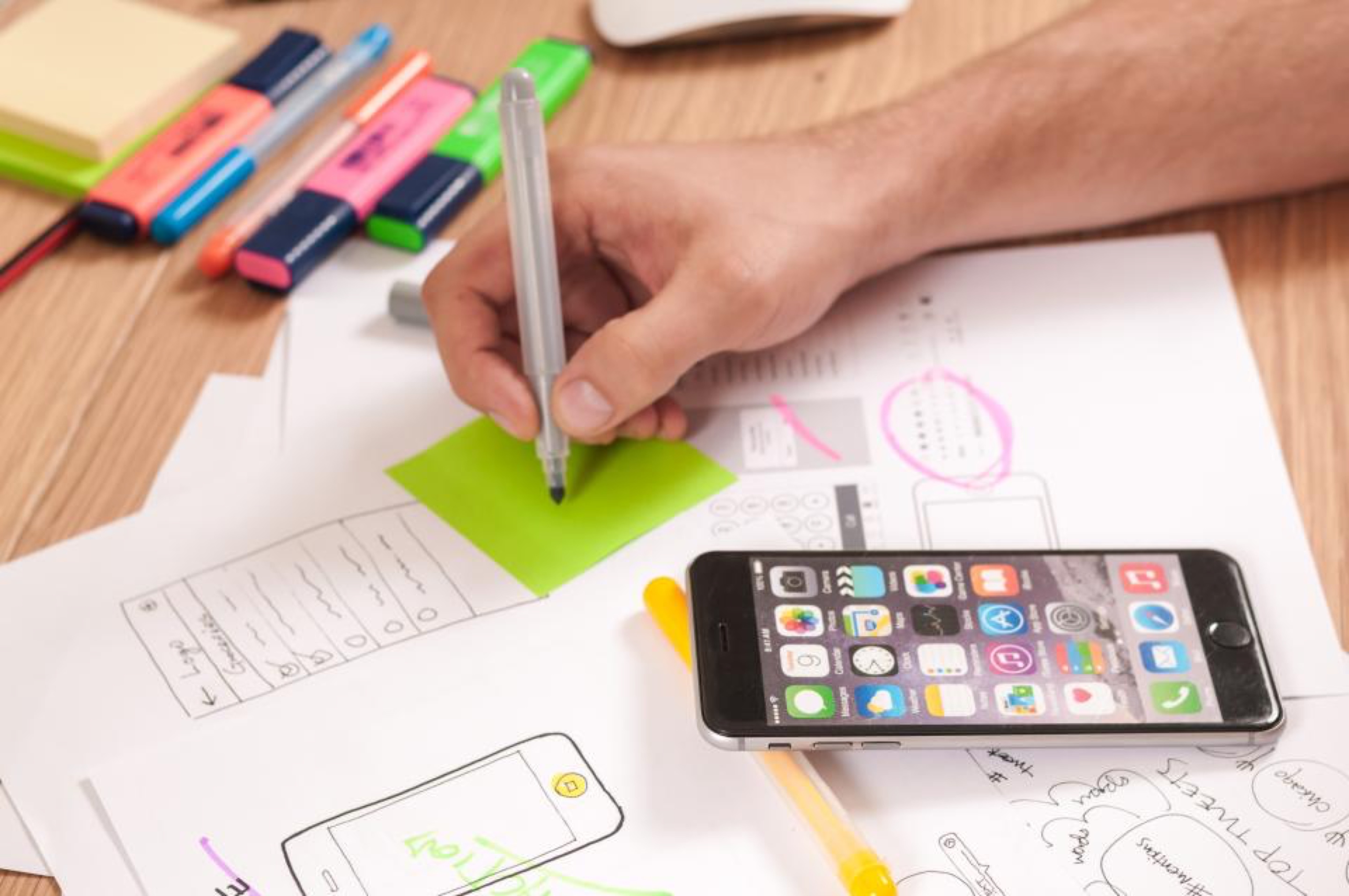Croquis d'écrans d'application sur papier, à côté d'un smartphone et de surligneurs.