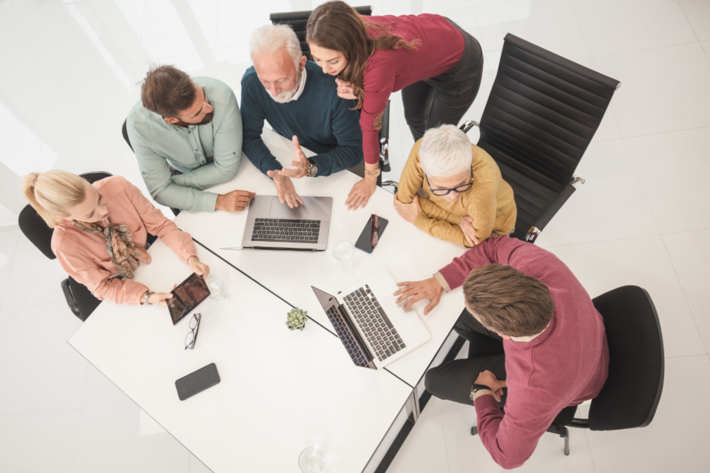 Équipe réunie autour d'une table blanche avec des ordinateurs portables, vue du dessus.